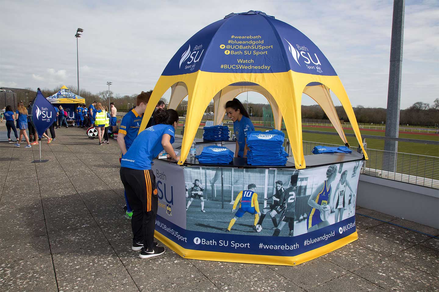 A big dome pop up banner branded with blue and yellow colours, with a woman inside promoting Bath SU sport and handing out branded t-shirts